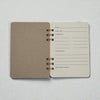 Open spiral-bound cocktail recipe journal with chipboard cover and ivory recipe pages