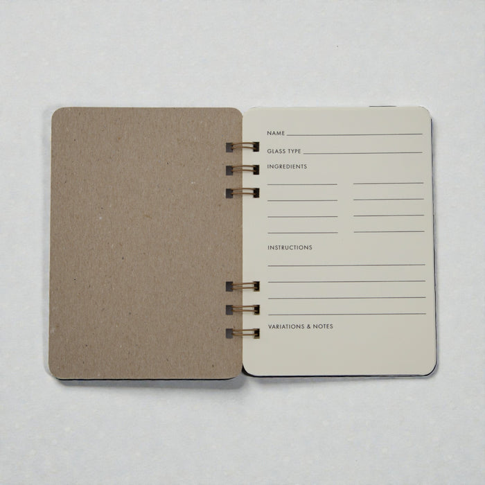 Open spiral-bound cocktail recipe journal with chipboard cover and ivory recipe pages